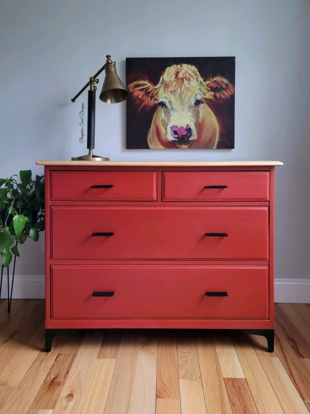 Bright red painted dresser with modern black pull handles and cow wall art
