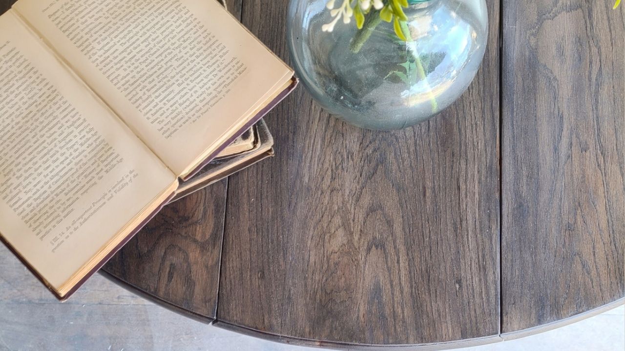 Flatlay of stained wood round table top with old books laying open on it and a blue glass vase